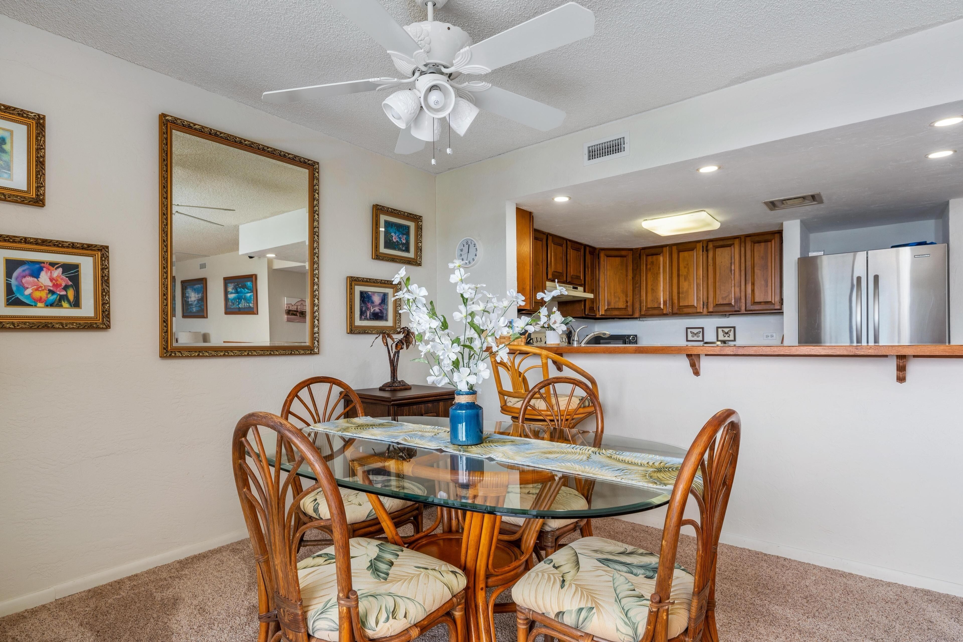 A dining area with a glass table, wooden chairs, and a ceiling fan.