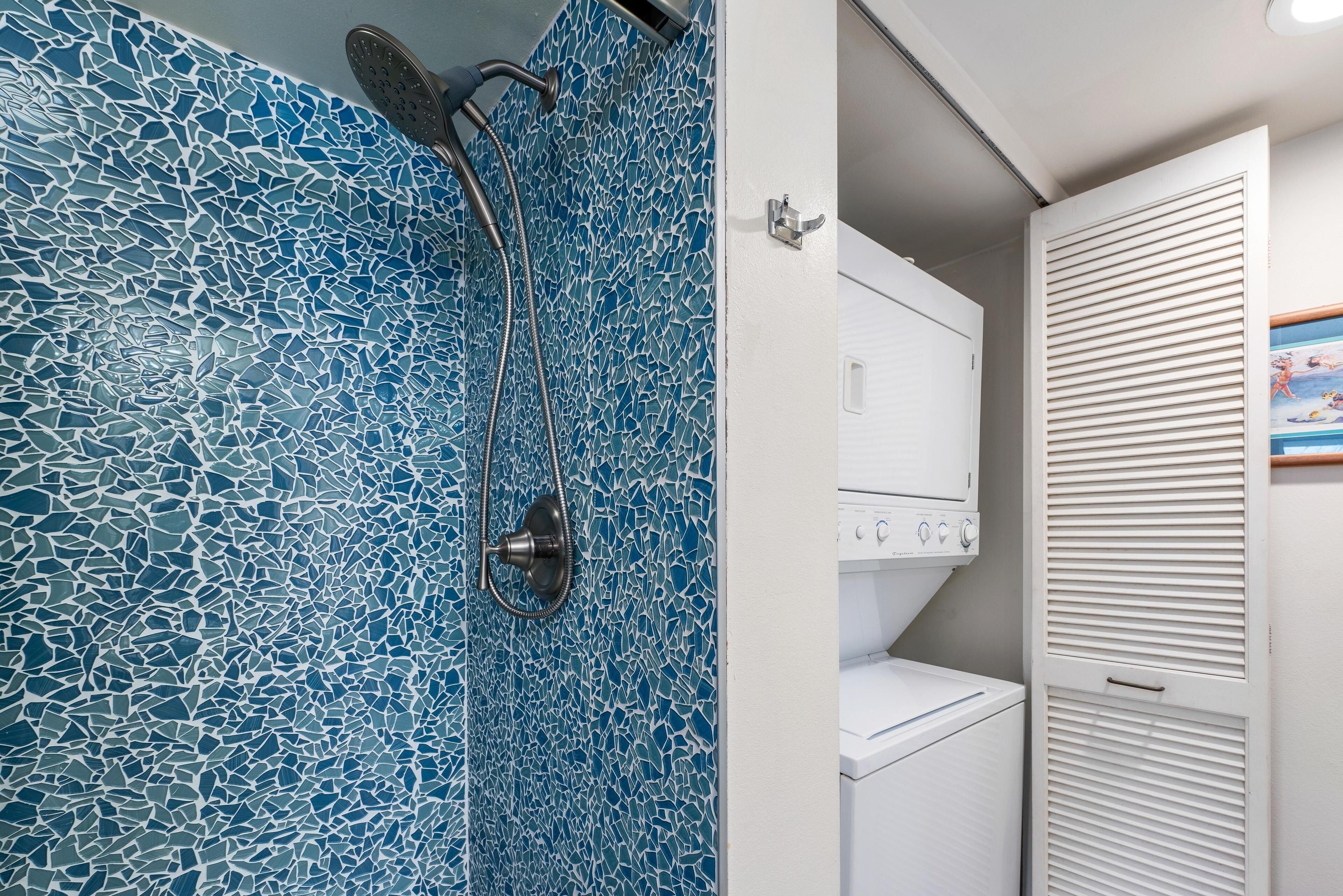 A bathroom with a mosaic tile shower wall, a white washing machine, and a white wardrobe with louvered doors.