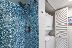 Un baño con pared de ducha de mosaicos, una lavadora blanca y un armario blanco con puertas persianas.