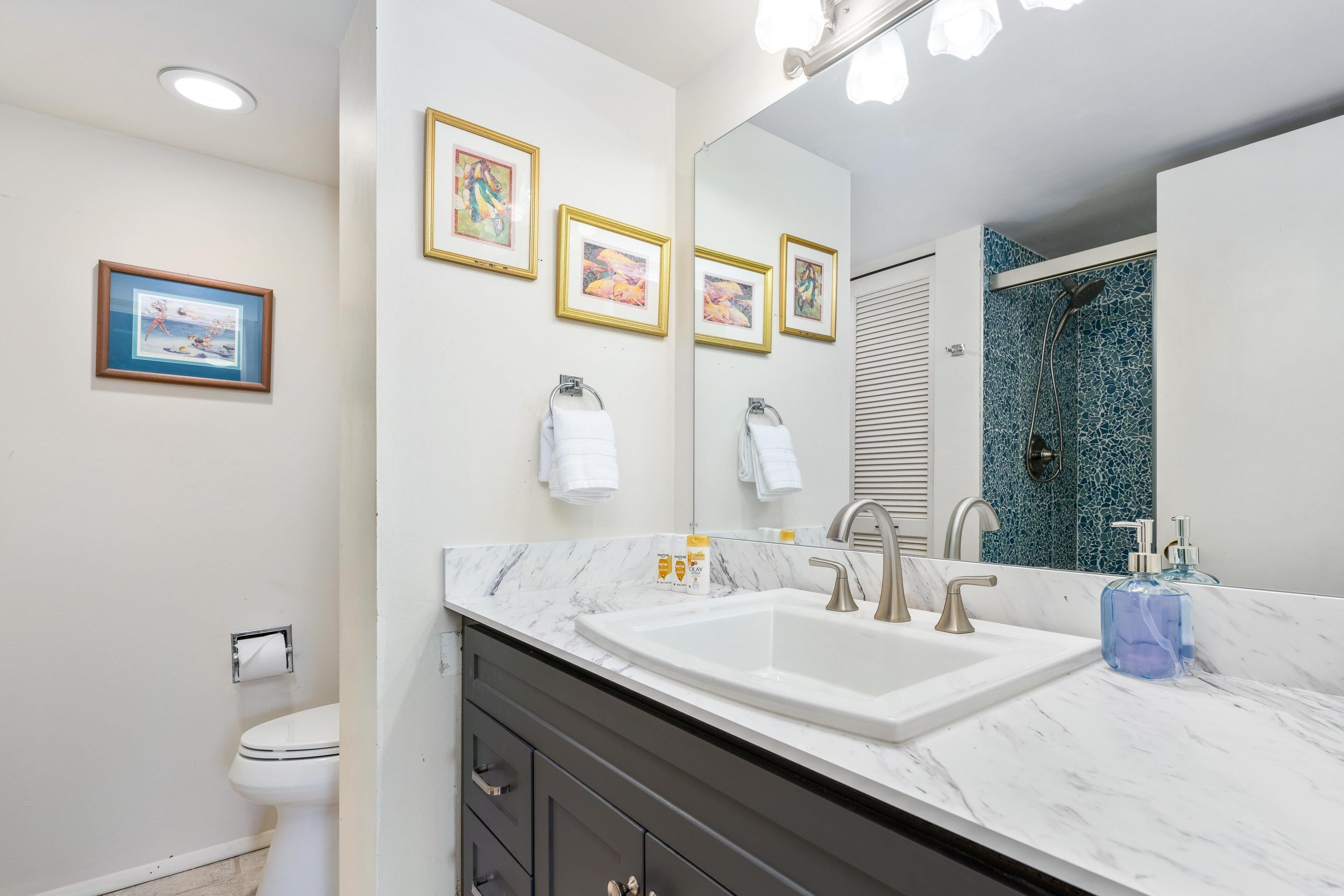 Une salle de bain moderne avec un grand lavabo, un miroir et des œuvres d’art encadrées accrochées au mur.