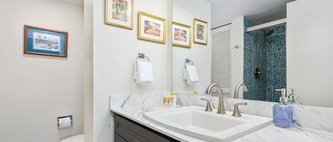 Une salle de bain moderne avec un grand lavabo, un miroir et des œuvres d’art encadrées accrochées au mur.