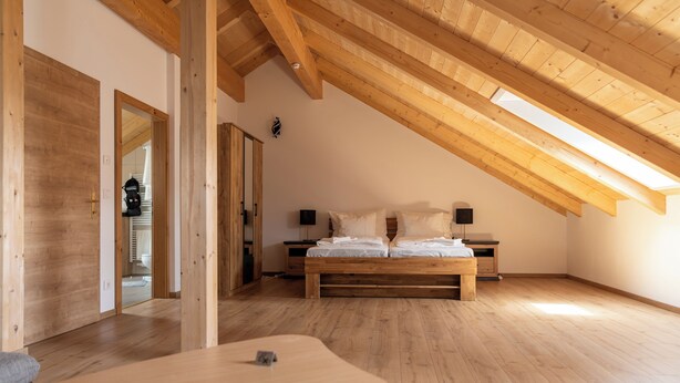 A bedroom with a sloped ceiling, wooden flooring, a bed with pillows, a bedside table, and a nightstand. - Ganzes Haus für den Gruppen- und Familienurlaub (Klagenfurt am Wörthersee)