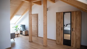 A room with a sloped ceiling, wooden beams, a bed, a wardrobe, a TV, and a plant. - Ganzes Haus für den Gruppen- und Familienurlaub (Klagenfurt am Wörthersee)