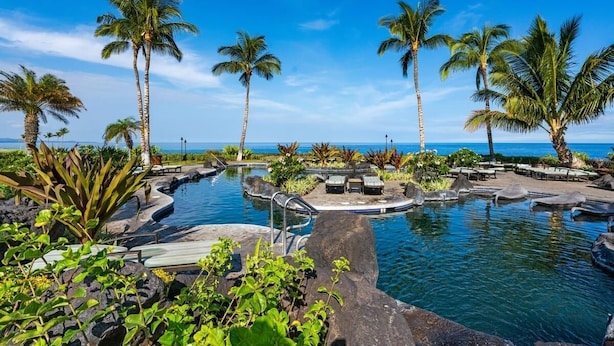 A pool area with palm trees, lounge chairs, and a view of the ocean.