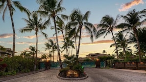 A paved entrance area with palm trees and a sign that reads "Hali'i Kai".