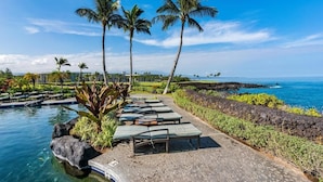 A poolside area with lounge chairs, palm trees, and a view of the ocean.