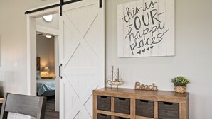 Une pièce avec une porte blanche, un lit recouvert d’une couverture bleue, une console en bois sur laquelle sont posés un modèle de bateau et une plante, et un panneau mural sur lequel on peut lire : « Ici, c’est notre havre de paix. »