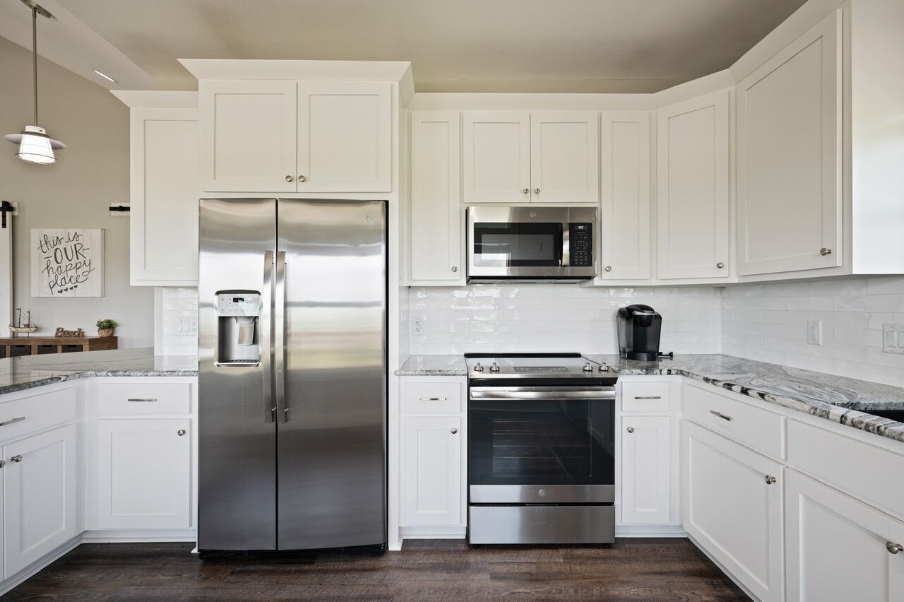 A modern kitchen with white cabinets, stainless steel appliances, and a marble countertop.
