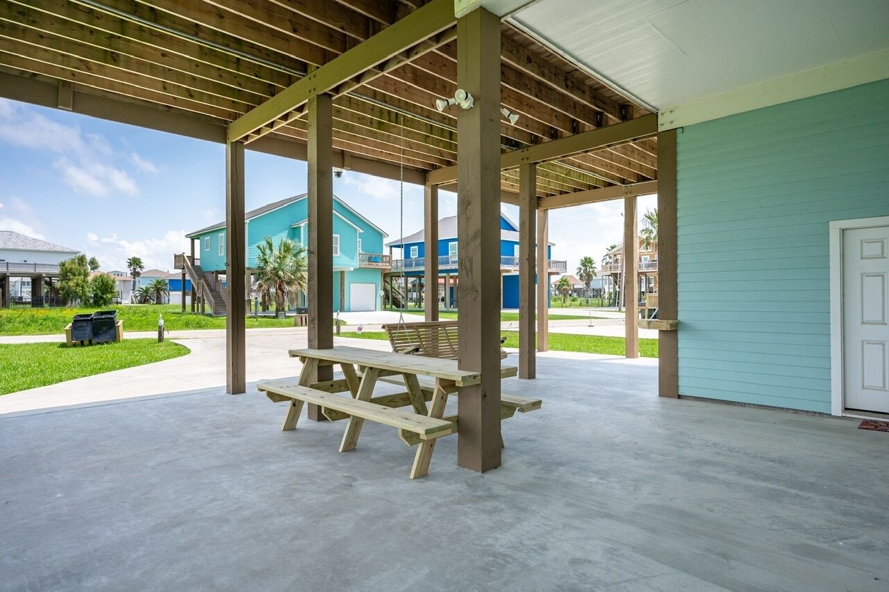 A covered outdoor area with a picnic table, wooden beams, and a view of buildings in the background.