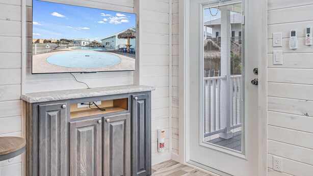 Ein Zimmer mit Fernseher, der Blick auf einen Pool bietet, einem Holzschrank und einer Tür mit Fenster.