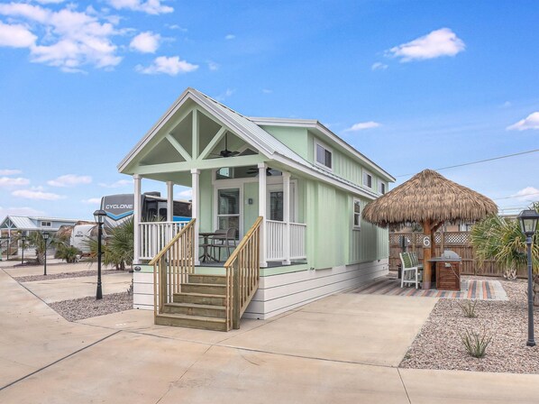 Situated on a concrete driveway, this single-story house features a porch with a thatched roof and wooden stairs.