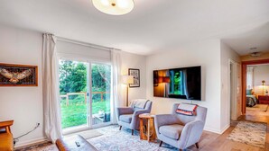 A spacious living room with a large window, two armchairs, a coffee table, and a flat-screen TV mounted on the wall. - Bay City Retreat ~ 1/2 Mi to Local Beach! (Bay City)