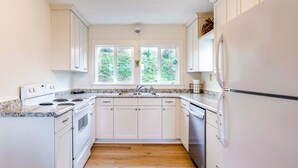 A kitchen with white cabinets, a granite countertop, a double sink, and a refrigerator. - Bay City Retreat ~ 1/2 Mi to Local Beach! (Bay City)