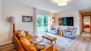 A living room with a sofa, armchairs, a coffee table, a TV, and a large window. - Bay City Retreat ~ 1/2 Mi to Local Beach! (Bay City)