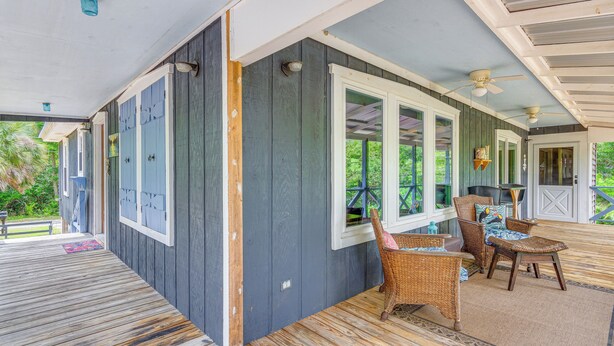 Une véranda couverte avec une terrasse en bois, des meubles en osier et un ventilateur de plafond.