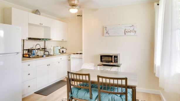 A kitchen with white cabinets, a microwave, a sink, and a dining area with a table and chairs.