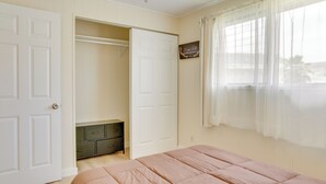A bedroom with a bed, a closet with hanging space, and a window with sheer curtains.
