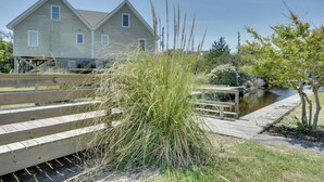 A two-story house with a dock extending into a body of water, surrounded by natural vegetation. - Buxton Vacation Rental w/ Shared Canal Access! (Buxton)