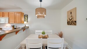A modern kitchen with wooden cabinets, a white dining table, and a hanging light fixture. - Buxton Vacation Rental w/ Shared Canal Access! (Buxton)