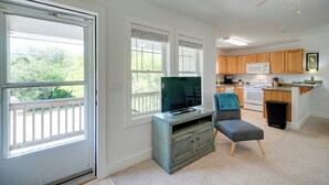A spacious living room with a television on a stand, a grey ottoman, and a balcony with a white railing. - Buxton Vacation Rental w/ Shared Canal Access! (Buxton)