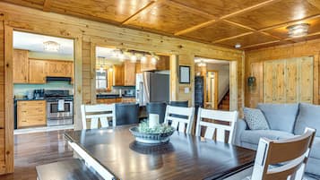Um interior em madeira com uma mesa de jantar, cadeiras, um sofá e uma cozinha com armários e eletrodomésticos.