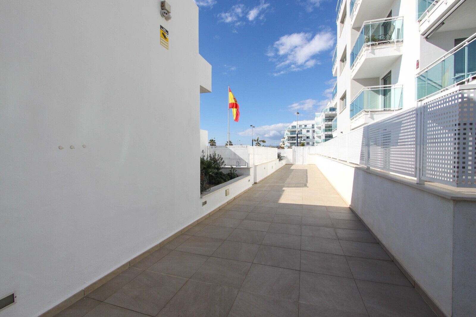 A narrow corridor with a tiled floor, white walls, and a flagpole with a flag.