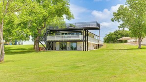 Une maison moderne à deux étages, dotée d’un balcon, entourée d’une pelouse bien entretenue et d’arbres.
