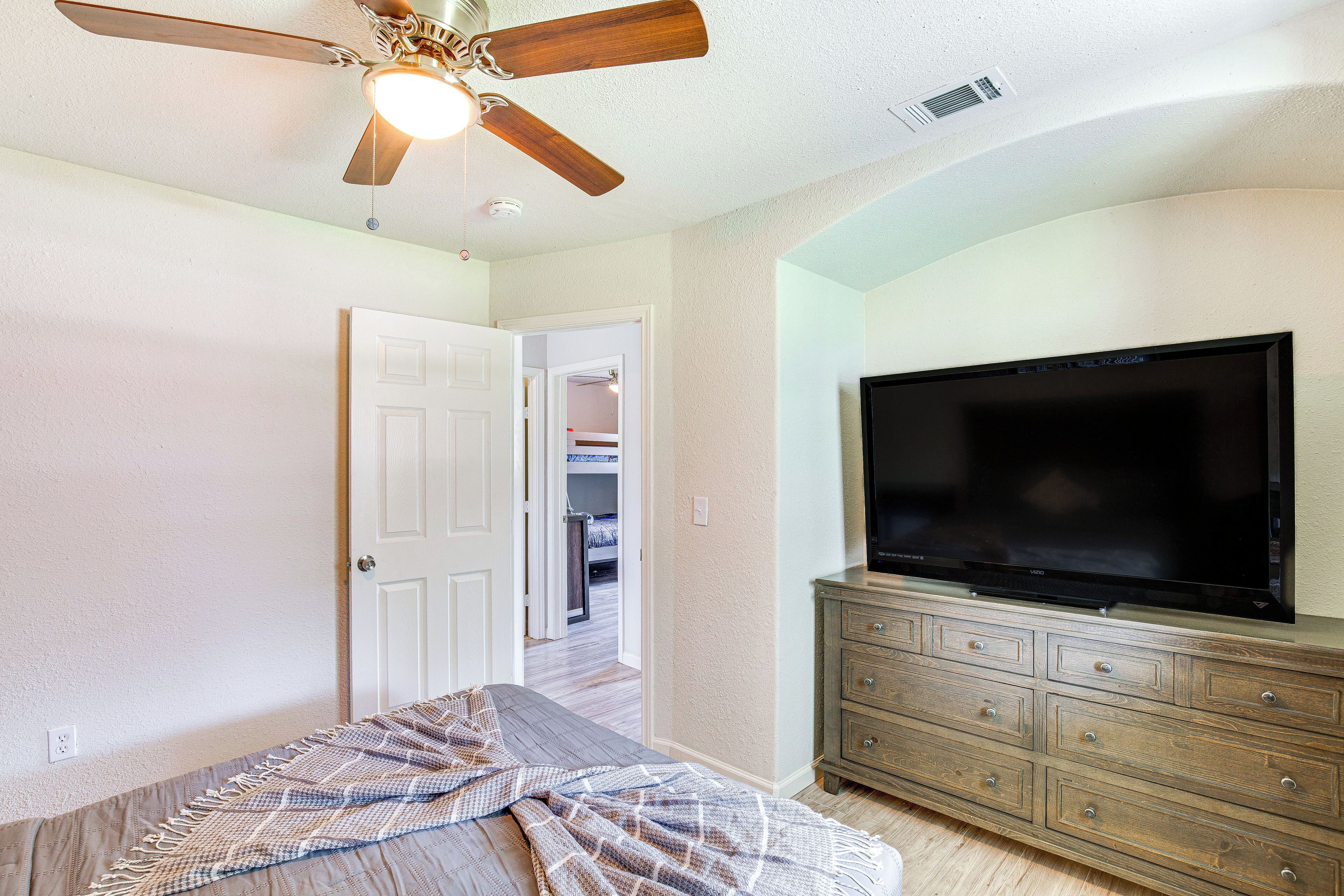 A bedroom with a bed, a ceiling fan, a television on a dresser, and a door leading to another room.