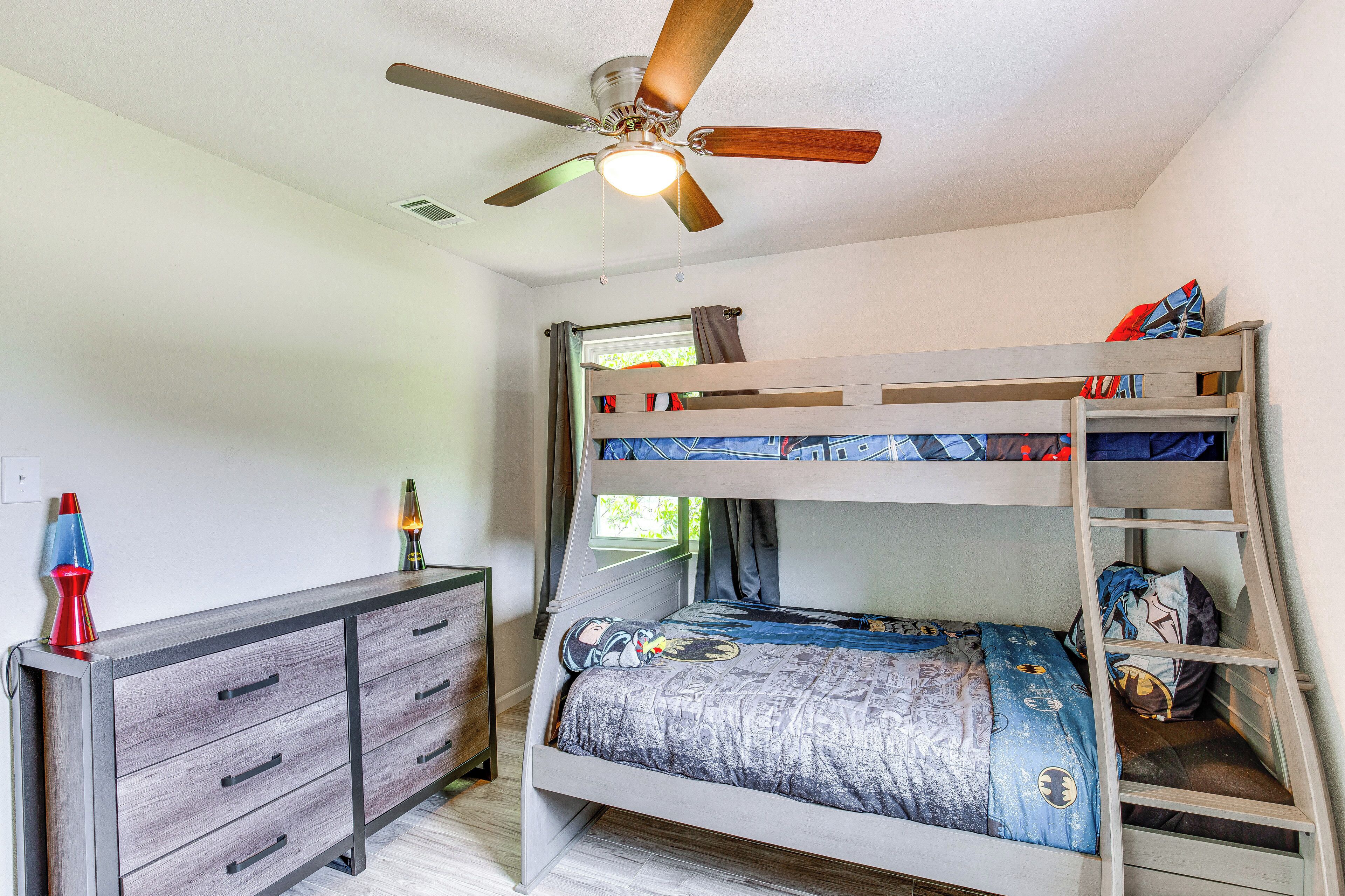 Una cama individual superpuesta con ventilador de techo, un aparador con cajones y una ventana con cortinas.