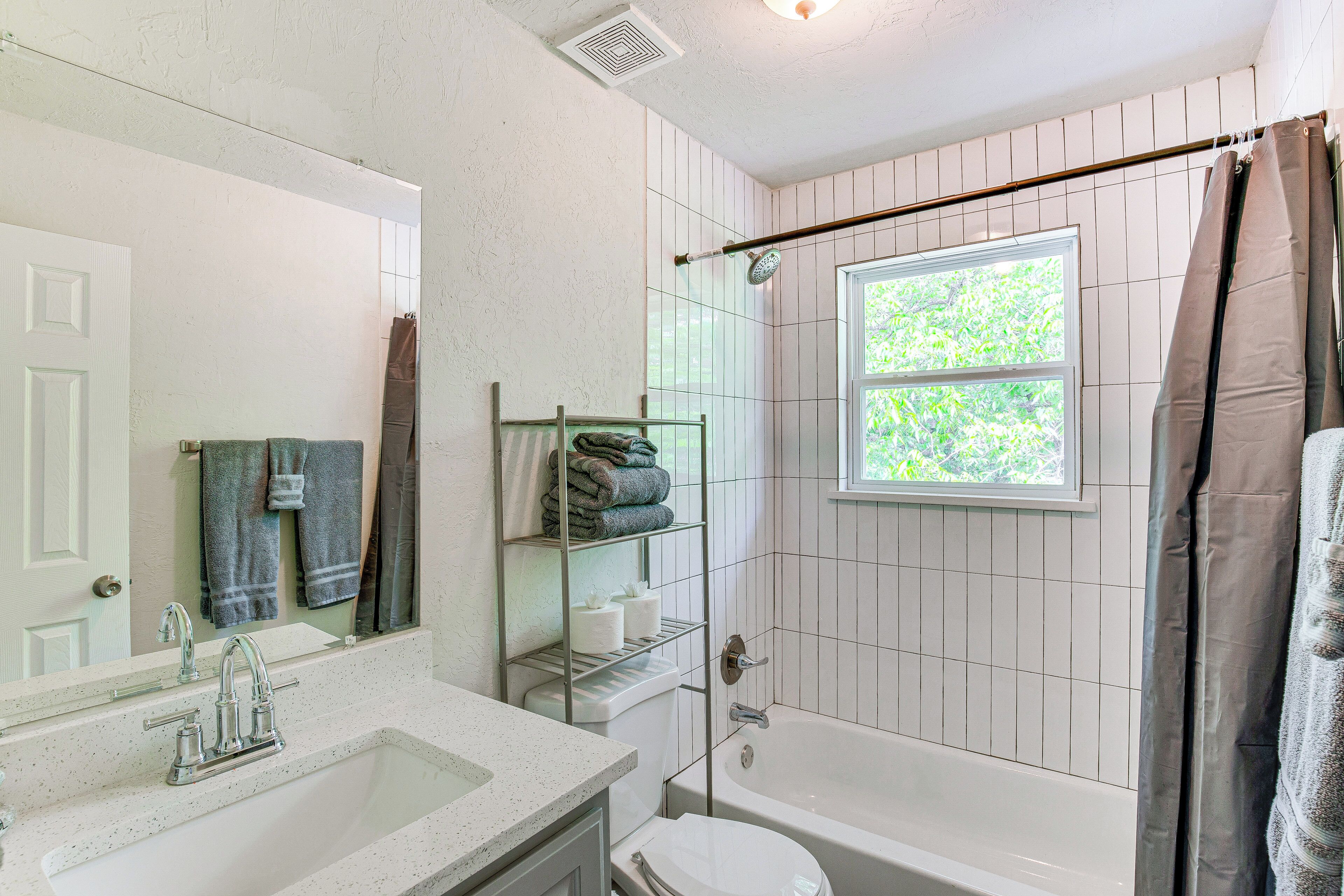 A bathroom with a white sink, a mirror, a shower with a window, and a towel rack.