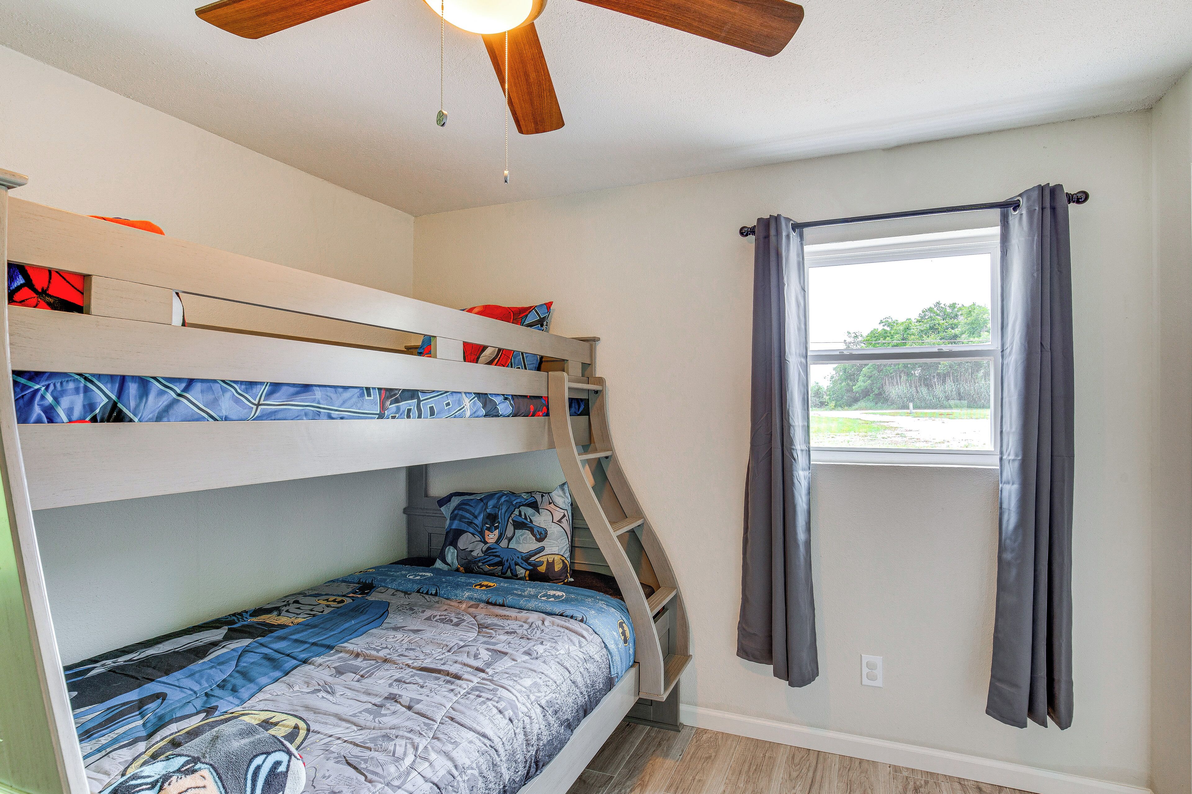 Une chambre avec un lit superposé, un ventilateur de plafond, une fenêtre avec des rideaux et une vue sur la verdure à l’extérieur.