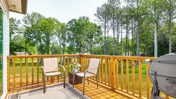 A wooden deck with two chairs and a grill, overlooking a grassy area with trees. - Secluded Guntersville Home Near Lake & Marinas! (Guntersville)