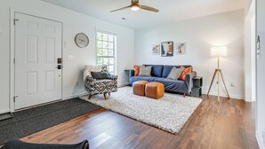 A living room with hardwood flooring, a white door, a patterned armchair, a blue sofa with orange cushions, a standing lamp, and a ceiling fan. - Secluded Guntersville Home Near Lake & Marinas! (Guntersville)