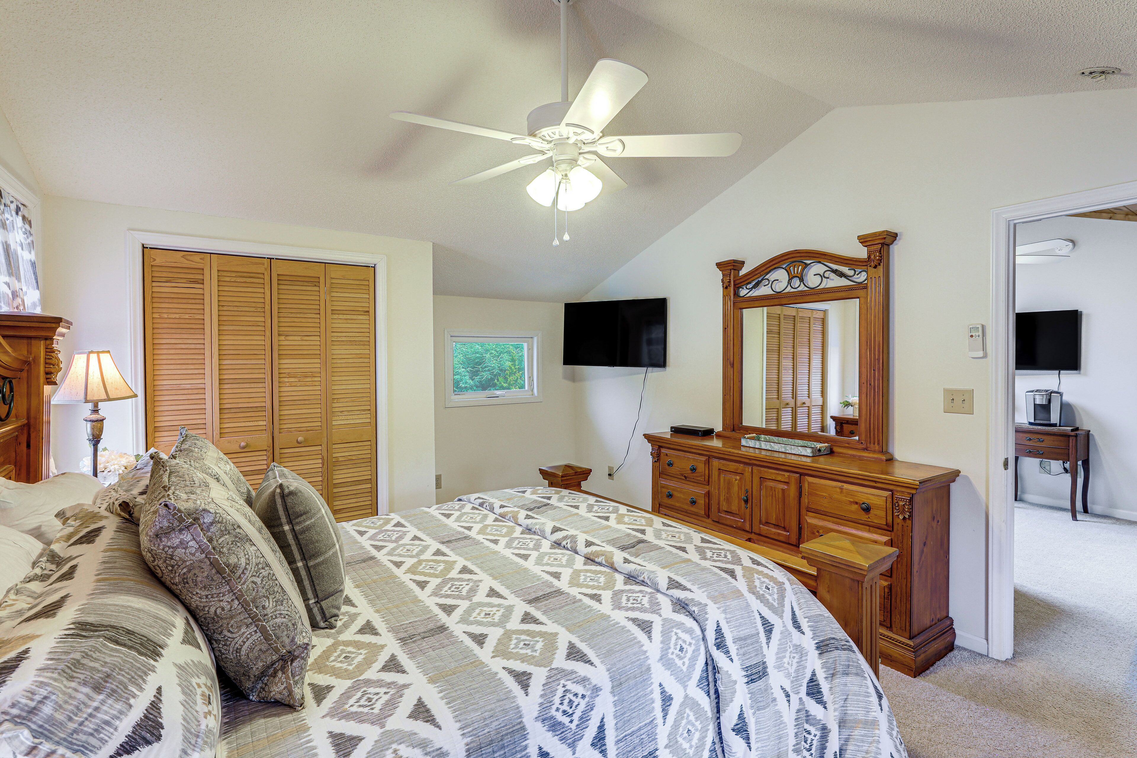 A bedroom with a bed, a ceiling fan, a dresser, a television, and a mirror.