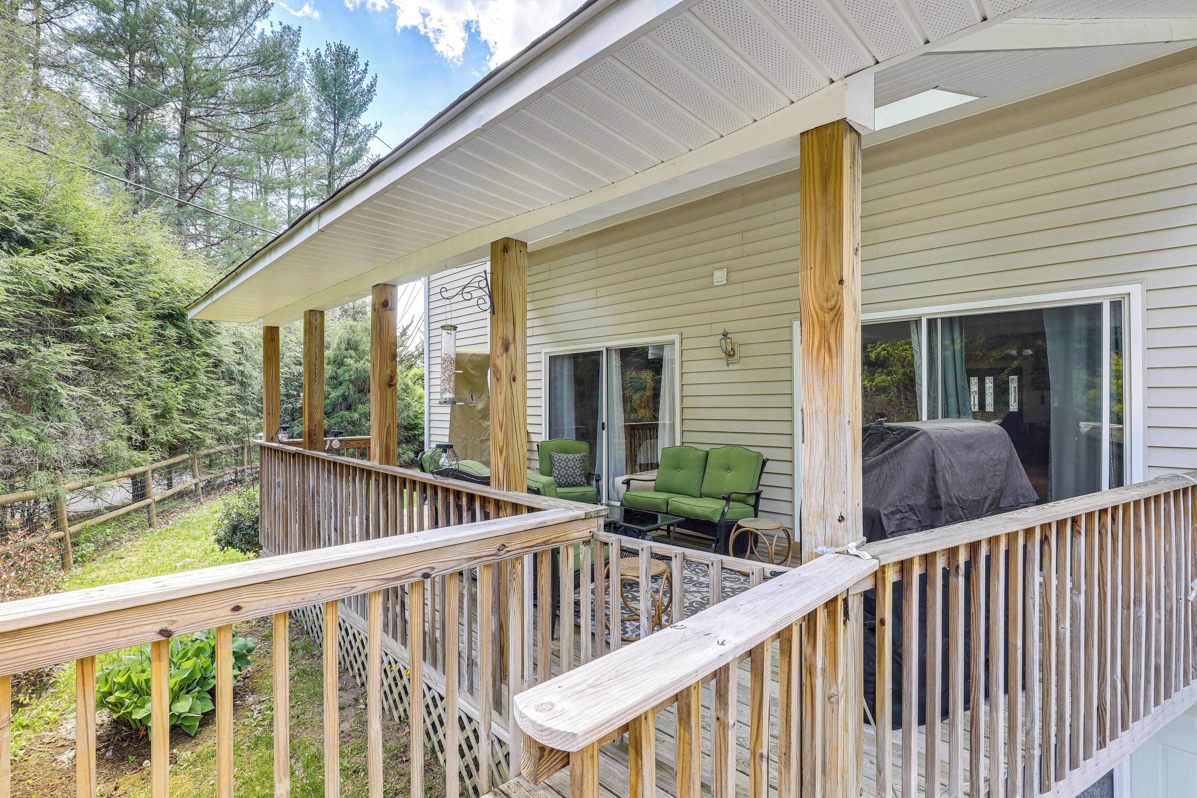 A wooden deck with a railing, a covered grill area, and a seating area with chairs.