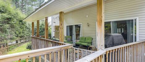A wooden deck with a railing, a covered grill area, and a seating area with chairs.