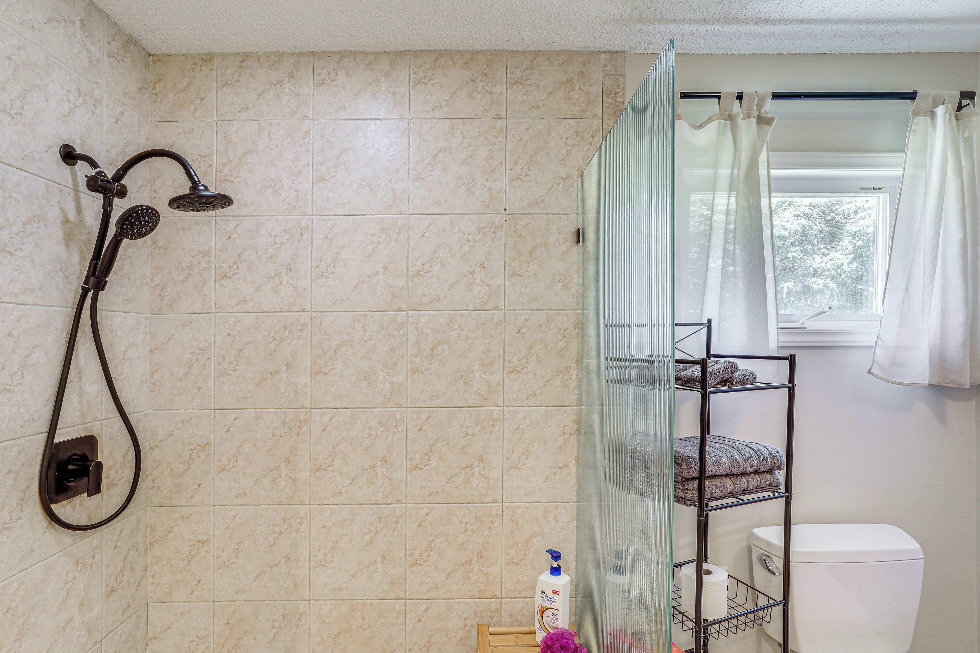 Ein Badezimmer mit Dusche, Toilette und einem Fenster mit Vorhängen.
