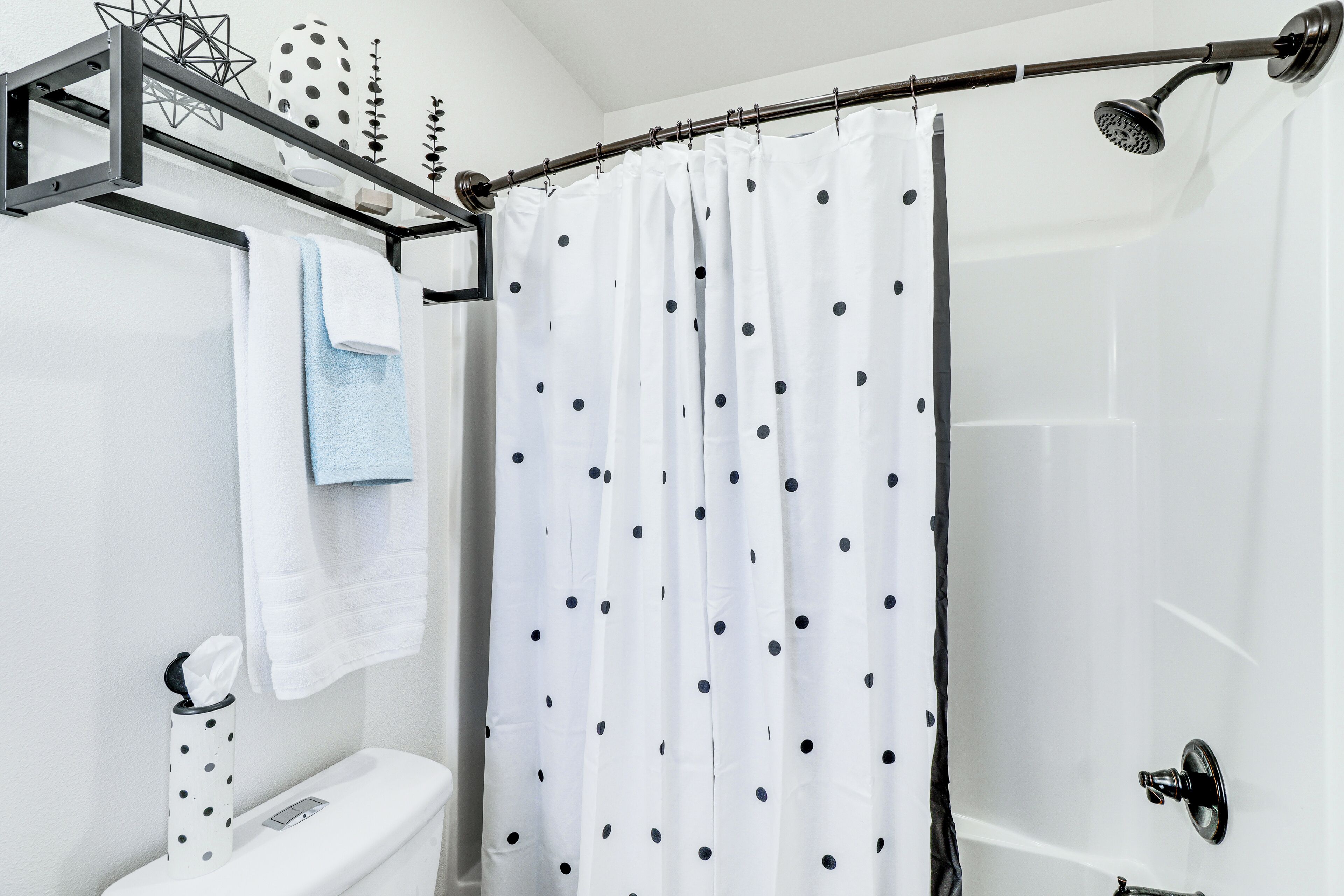 Une salle de bain avec un rideau de douche à motifs à pois, un porte-serviettes avec une serviette blanche et des toilettes dotées d’un distributeur d’essuie-tout.