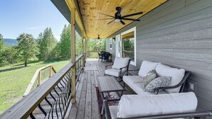 A covered porch with a ceiling fan, outdoor seating, and a view of the surrounding landscape.