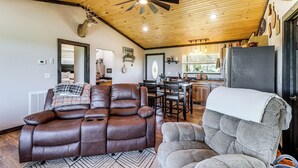 A spacious living area with a leather recliner, a gray armchair, and a ceiling fan.