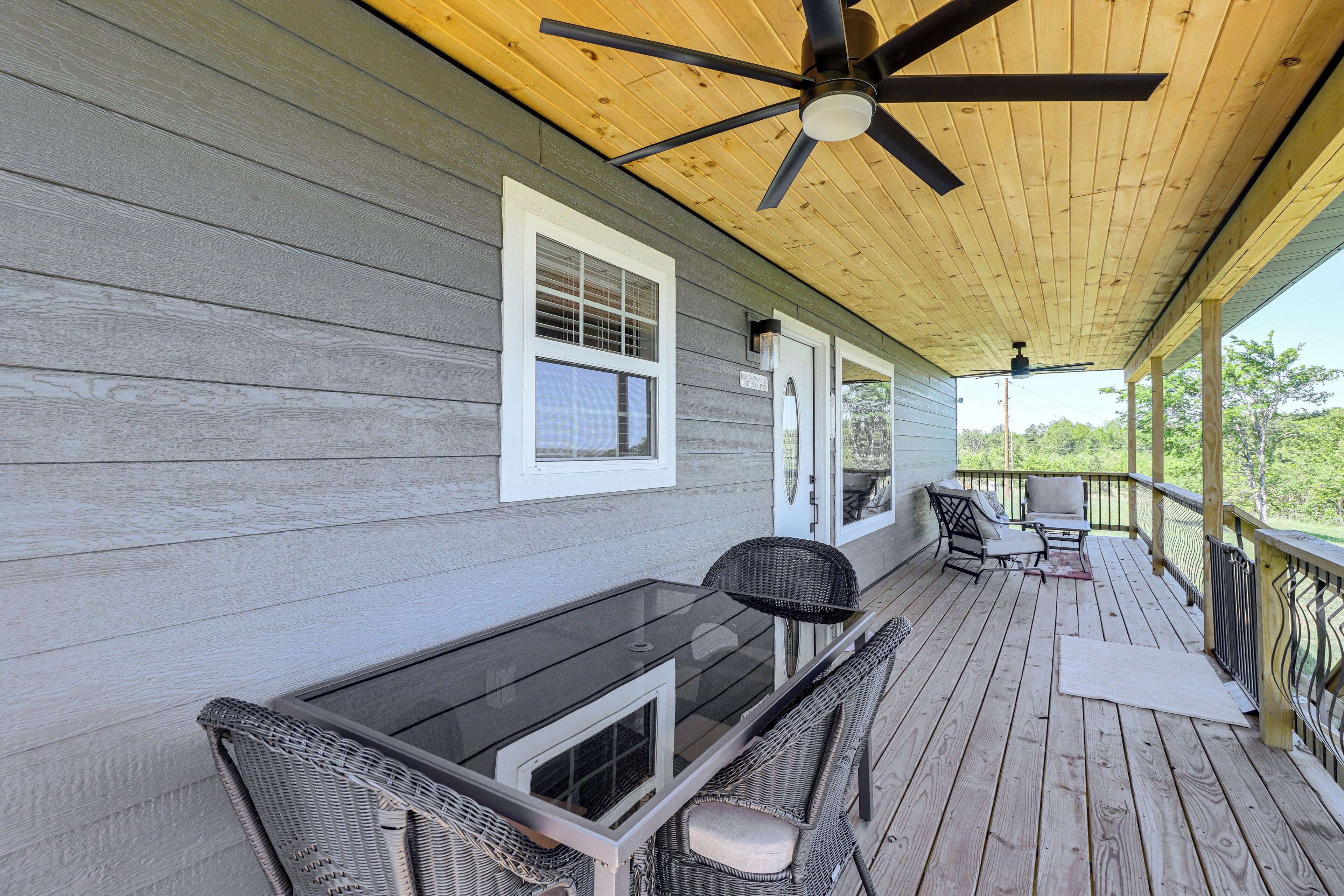 A covered porch with a glass-top table and wicker chairs, a ceiling fan, and a view of the outdoors.