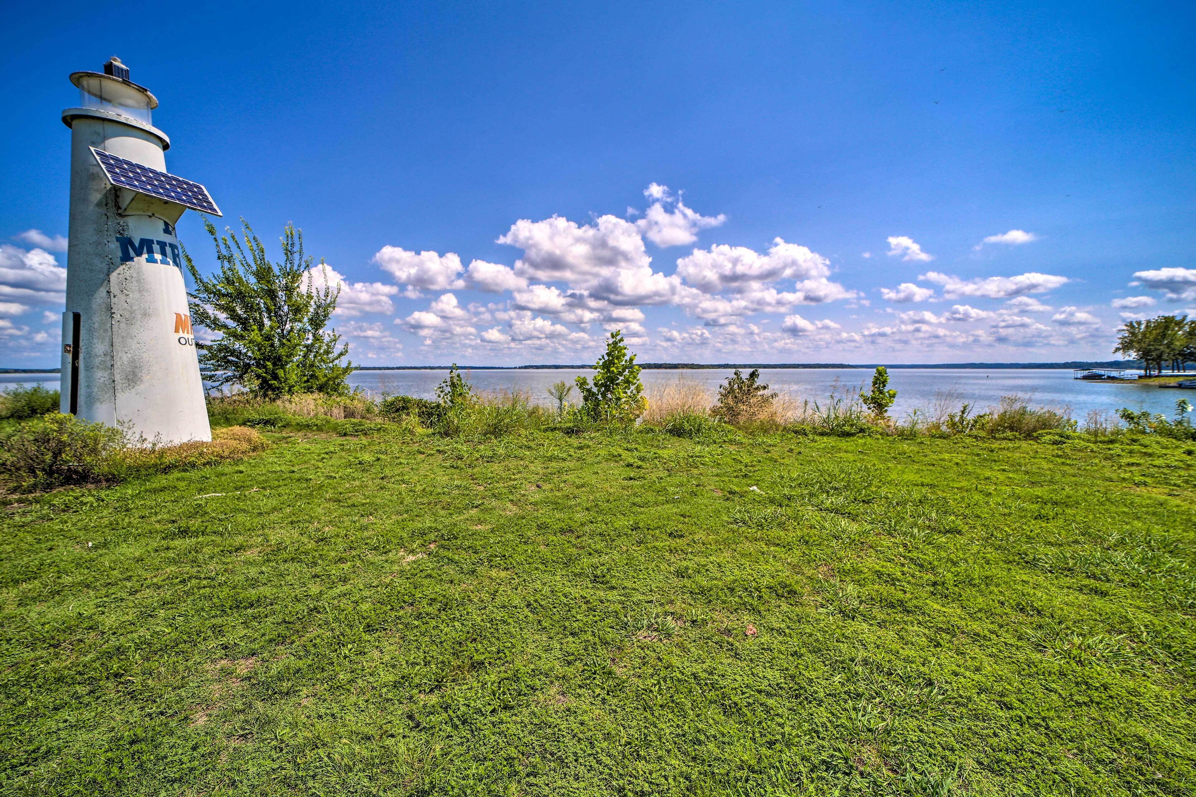 A lighthouse with solar panels, a grassy field, and a body of water with a clear sky.