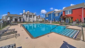 Une piscine avec des chaises longues, un espace de détente couvert et un bâtiment rouge doté d’un porche.