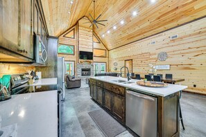 A spacious kitchen with a large island, wooden walls, and a stone fireplace. - Private Hot Tub: Luxe Cabin in Broken Bow! (Broken Bow)