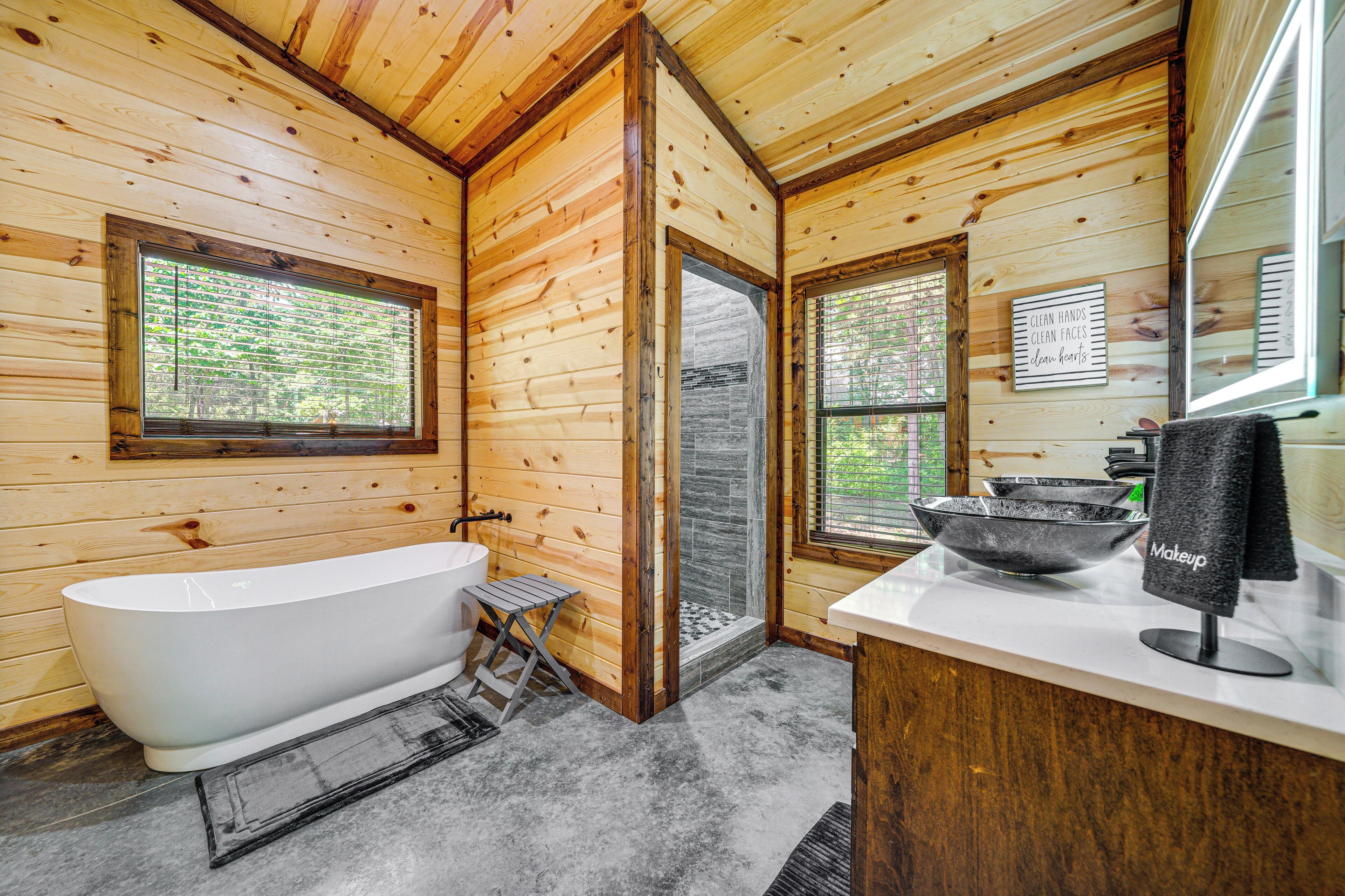 A wooden cabin bathroom with a freestanding bathtub, a shower, and a vanity with a bowl sink and a towel rack.