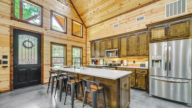 A modern kitchen with a large island, bar stools, stainless steel appliances, and wooden cabinetry. - Private Hot Tub: Luxe Cabin in Broken Bow! (Broken Bow)