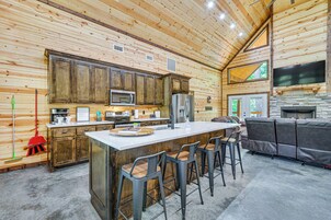 Una cocina moderna con armarios de madera, una isla central con taburetes de bar, horno empotrado y chimenea de piedra.