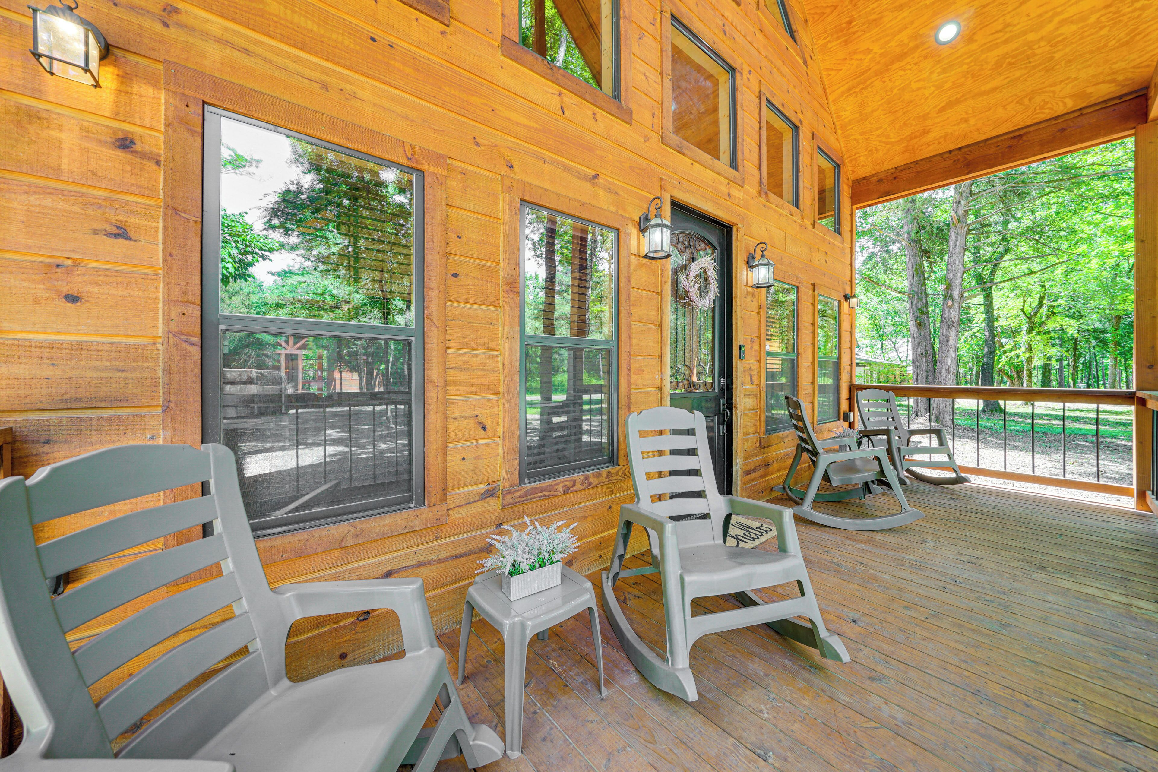 A wooden cabin with large windows, rocking chairs, and a small table with a plant.
