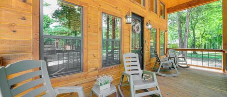 A wooden cabin with large windows, rocking chairs, and a small table with a plant.