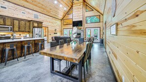 A spacious wooden cabin with a large dining table, bar area, and a cozy living room with a fireplace. - Private Hot Tub: Luxe Cabin in Broken Bow! (Broken Bow)